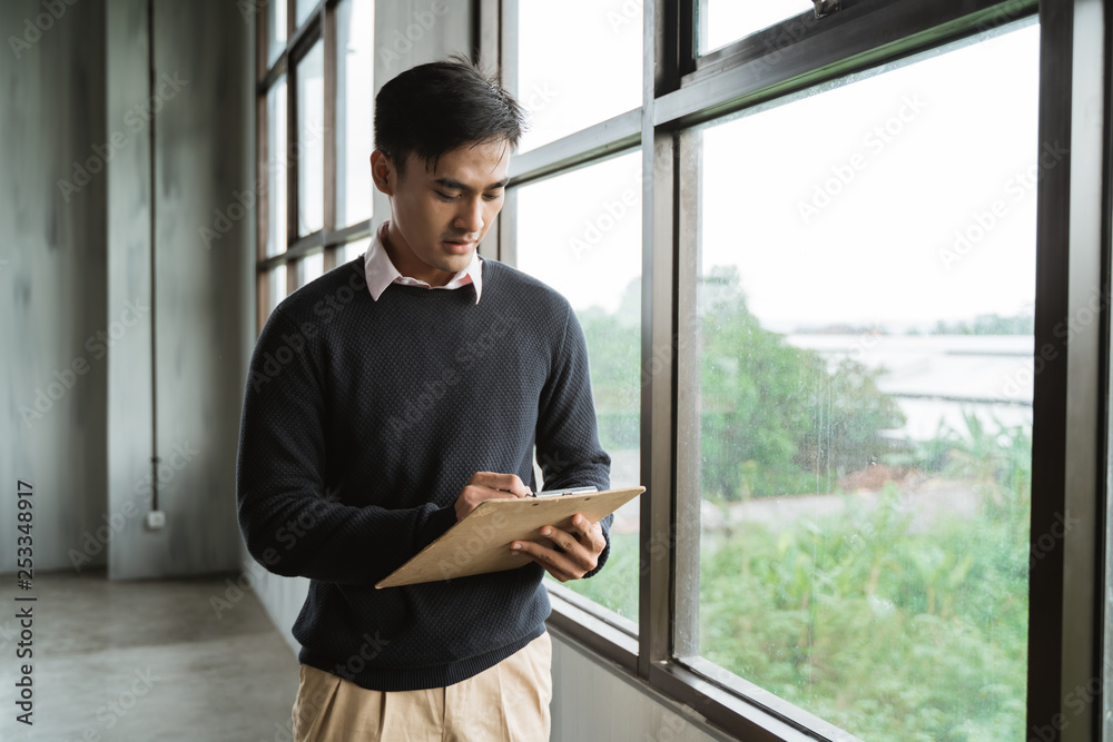 portrait of a man serious write on clipboard when standing in the office room near windows portrait of a man serious write on clipboard when standing in the office room near windows