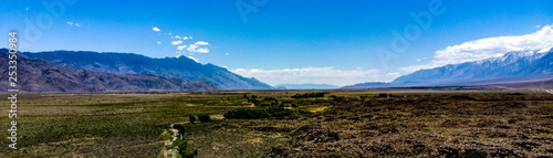 Aerial, drone view of Owens Valley and the snowcapped Eastern Sierra Nevada Mountains along California State Highway 395 in the spring with blue sky, white clouds, purple mountains and green flora