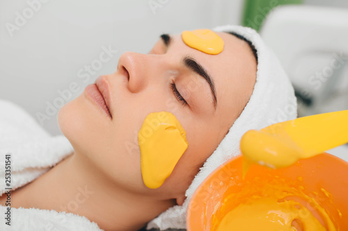 Beautician applying facial mask with orange extract on beautiful female face