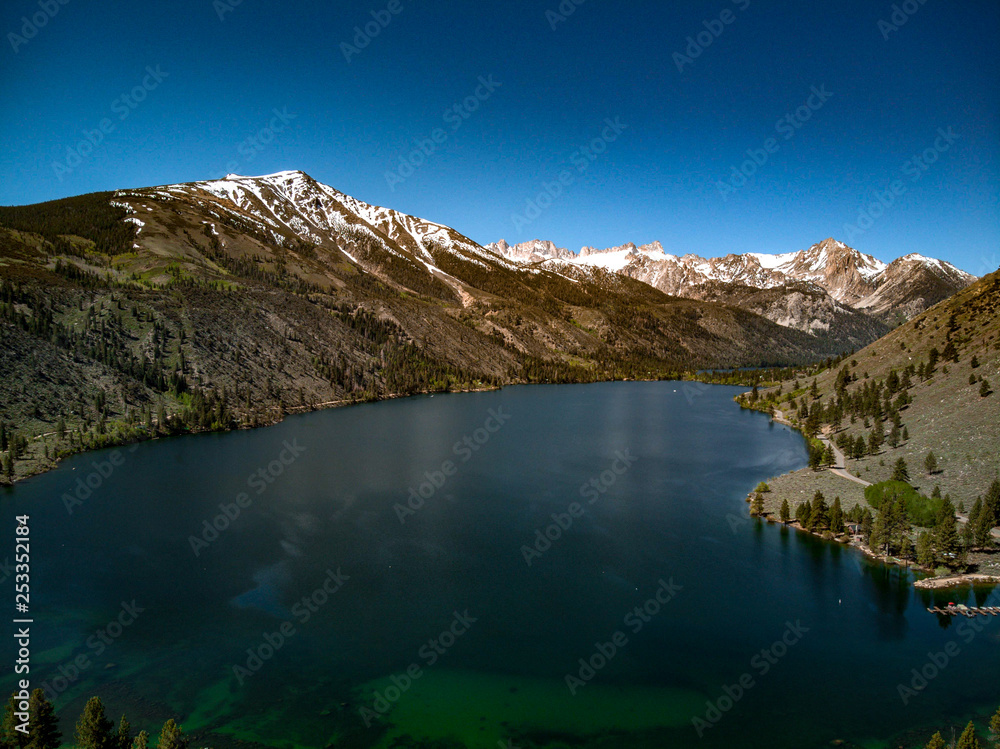 Aerial, drone view of Twin Lakes in the Eastern Sierra Nevada Mountains near Yosemite in Mono County, California with clear blue sky and water, snow capped mountain peaks, green hill sides Aerial, drone view of Twin Lakes in the Eastern Sierra Nevada Mountains near Yosemite in Mono County, California with clear blue sky and water, snow capped mountain peaks, green hill sides