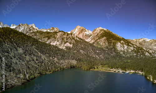 Aerial, drone view of Twin Lakes in the Eastern Sierra Nevada Mountains near Yosemite in Mono County, California with clear blue sky and water, snow capped mountain peaks, green hill sides
