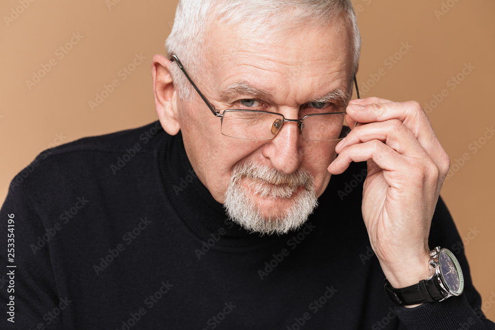 Obraz premium Old attractive man with gray hair and beard in eyeglasses and sweater dreamily looking in camera over beige background isolated
