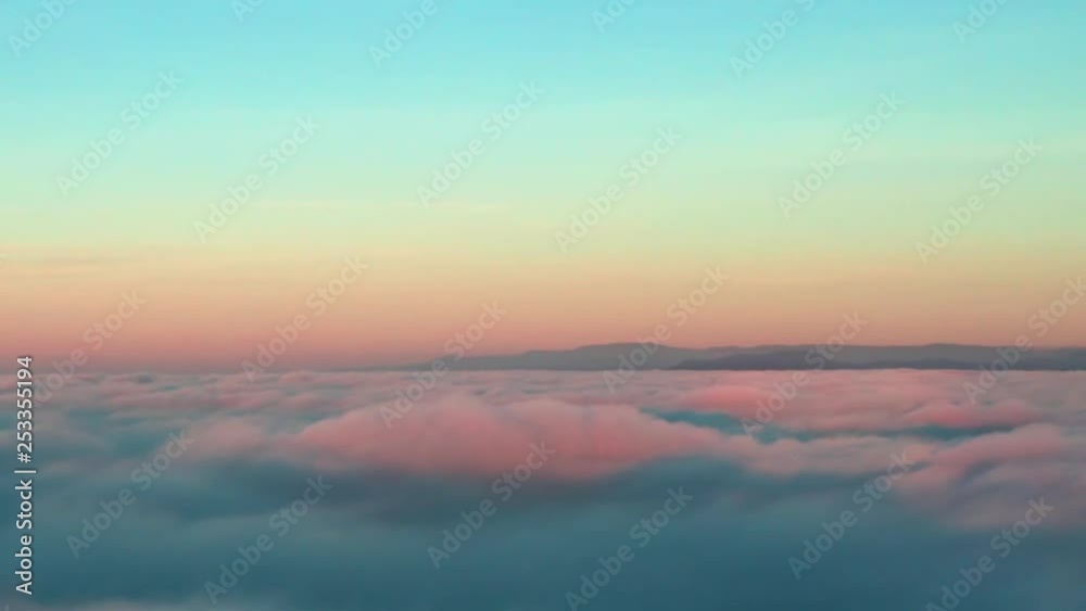 Aerial rising shot above fluffy cloud inversion illuminated by the sunset with mountain ranges in the distance. Aerial rising shot above fluffy cloud inversion illuminated by the sunset with mountain ranges in the distance.