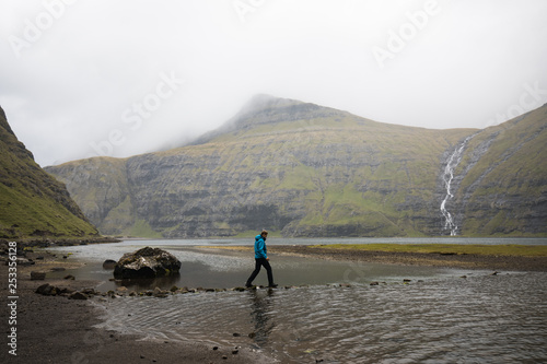Man treading carefully over stones in a river on hike to reach waterfall in Faroe Islands 