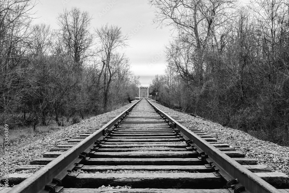 Black and white train tracks with a bridge in distance.