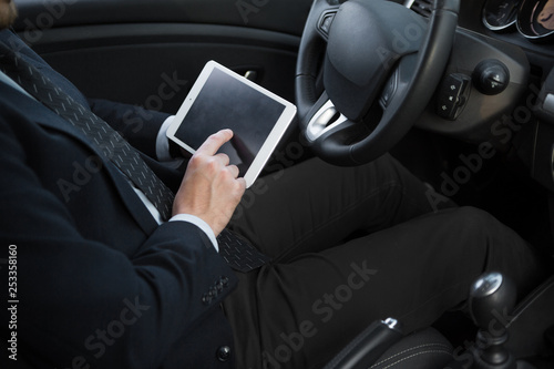 Side view of confident senior man in formalwear sitting in car and hold tablet pc