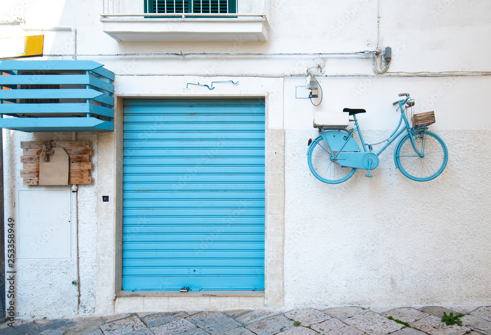 A blue door and a turquoise blue bicycle hanging on the wall in the old town of Monopoli, Puglia, Italy. A region of Apulia. Colorful house and street A blue door and a turquoise blue bicycle hanging on the wall in the old town of Monopoli, Puglia, Italy. A region of Apulia. Colorful house and street
