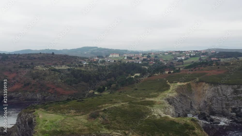 Aerial low drone flight over the tree crones to the little village located on grassy hills; extremely near view from above of winter countryside life; foggy day in Spain north; beautiful rural scene