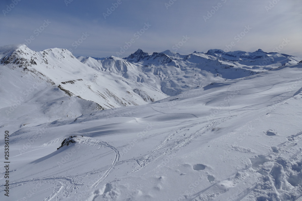 snowy ski slope with print from skis, snowboards and foot, snow mountains and blue sky with clouds