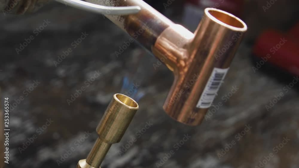 Solder being melted on a copper tee connection while it's being heated by a propane blow torch. Extreme closeup. Solder being melted on a copper tee connection while it's being heated by a propane blow torch. Extreme closeup.