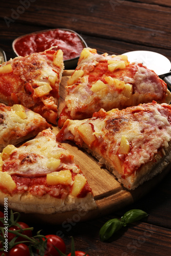 Delicious pizza with pineapple, ham slice, bacon slice, mozzarella cheese, pizza sauce on rustic background for fast food and ready to eat concept