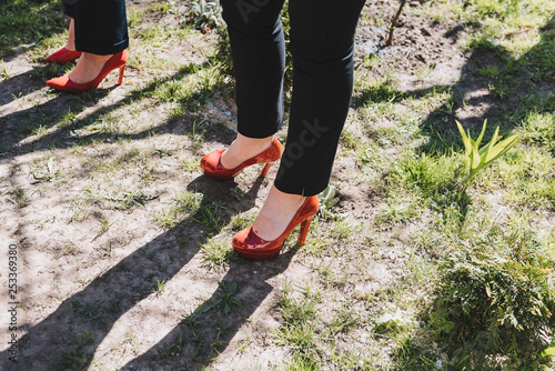 Women wearing black pants and red high heeled shoes standing on the ground