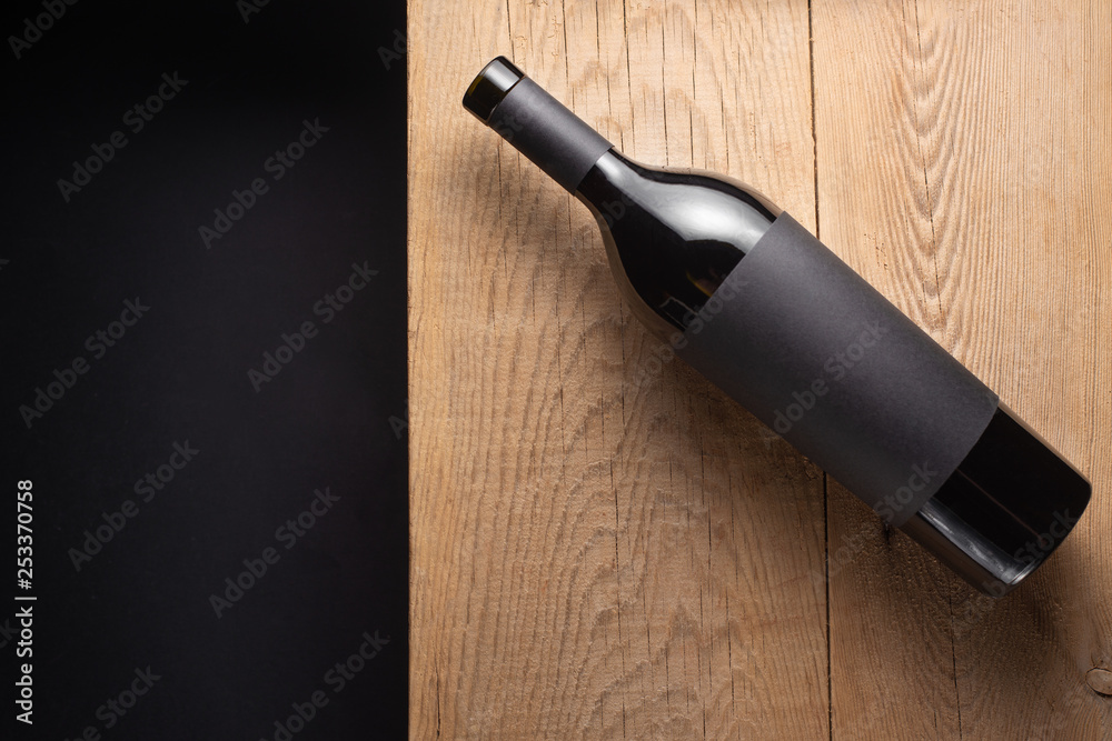 Fototapeta premium Bottle of red wine with black blank label on the old board. A mock up bottle of wine. View from above. Flat lay. Black background space