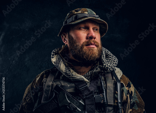 Portrait of a special forces soldier in the military camouflaged uniform, looking sideways. Studio photo against a dark textured wall 
