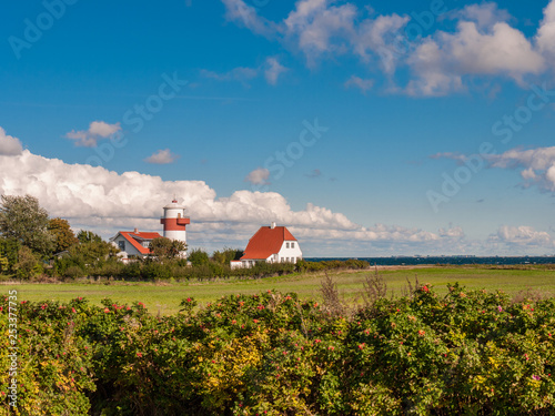 Small red and white colored lighthouse with a field in front of a wild blue sky near Lohals on Langeland island, Denmark