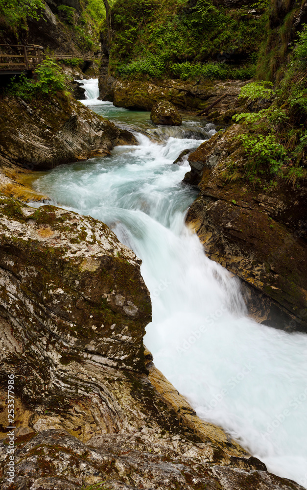 Naklejka premium Wood walkway over turquoise waterfalls and rapids on Radovna river Vintgar Gorge forest with sedimentary limestone rock layers Slovenia