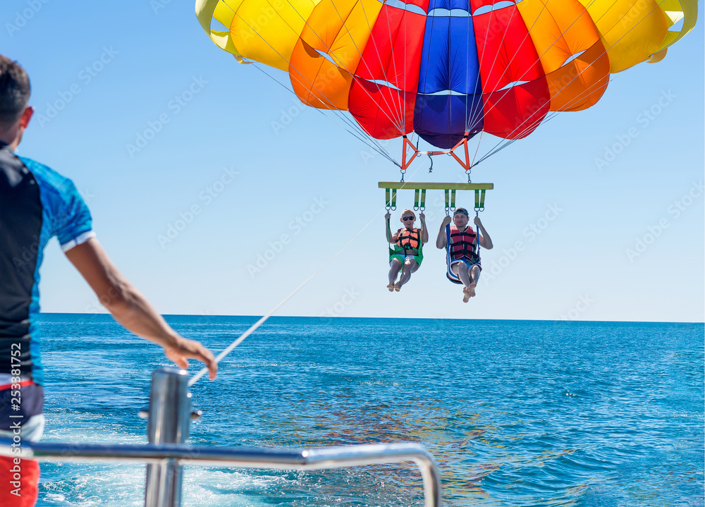 Happy couple Parasailing on Miami Beach in summer. Couple under parachute hanging mid air. Having fun. Tropical Paradise. Positive human emotions, feelings, family, travel, vacation. - obrazy, fototapety, plakaty 