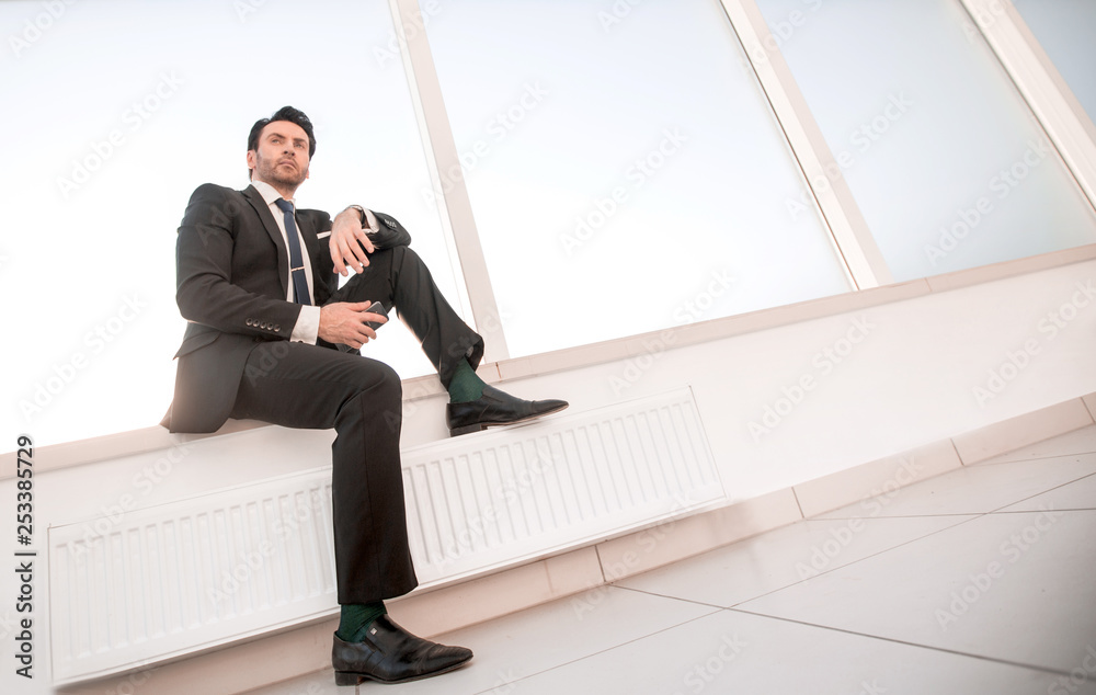 confident businessman with a smartphone sitting in the office hallway confident businessman with a smartphone sitting in the office hallway