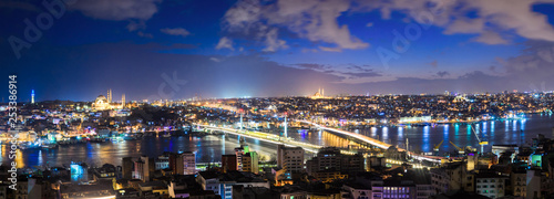 Panorama top view of illuminated Istanbul cityscape at night with Bosphorus between two shores and bridges over it. Many mosques and buildings are seen