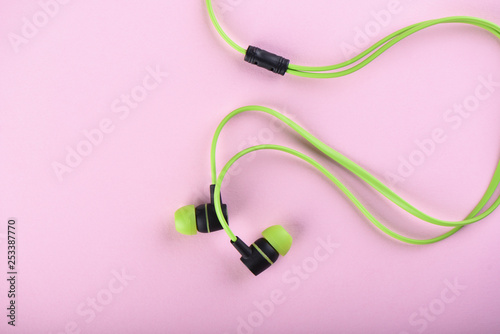 Green headphones or earphones isolated on a pink background