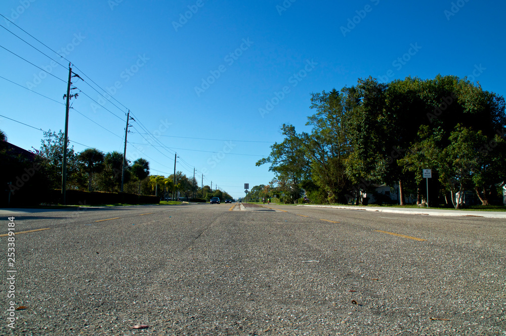A low angle view of Vanderbilt Drive road in Bonita Springs Florida, with cars and bicycles in the distance and a clear blue sky.