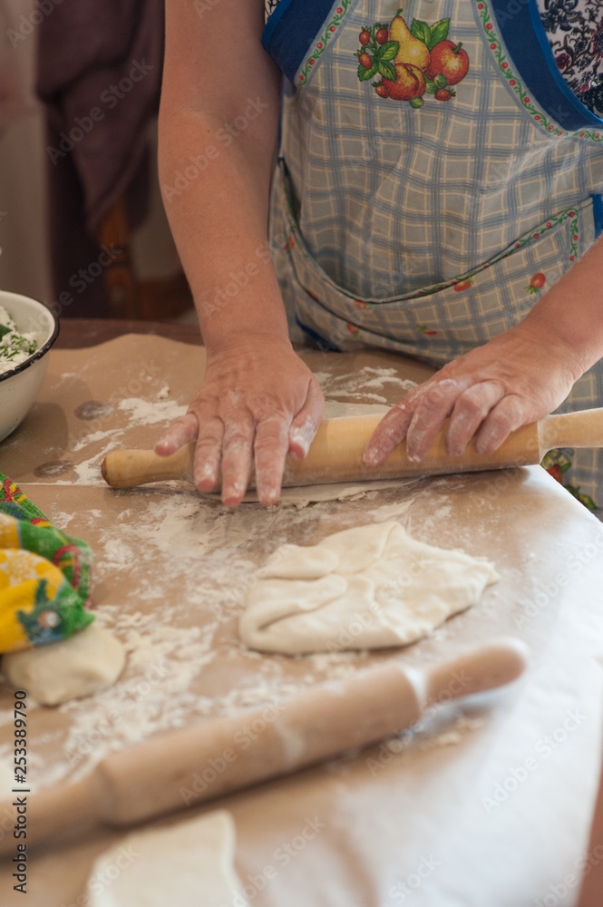Women's hands rolling dough with a rolling pin