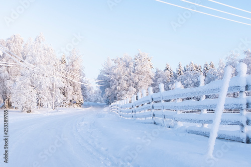 Snow-covered landscape, rural road and wooden fence in frost. Finland Lapland