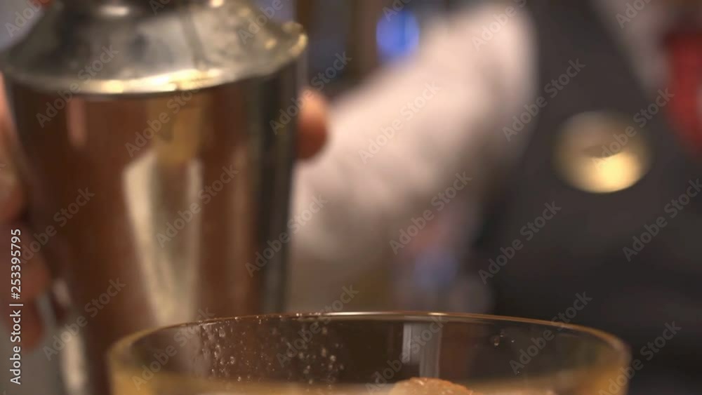 Yellow cocktail being poured from shaker into glass. Yellow cocktail being poured from shaker into glass.
