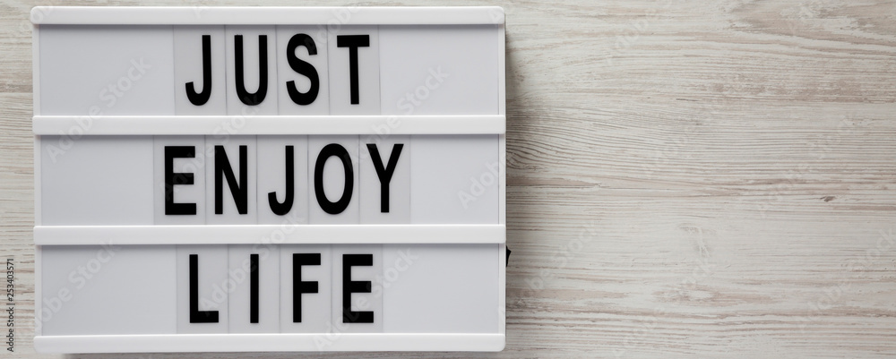 Obraz premium 'Just enjoy life' words on modern board on a white wooden surface, top view. Copy space.