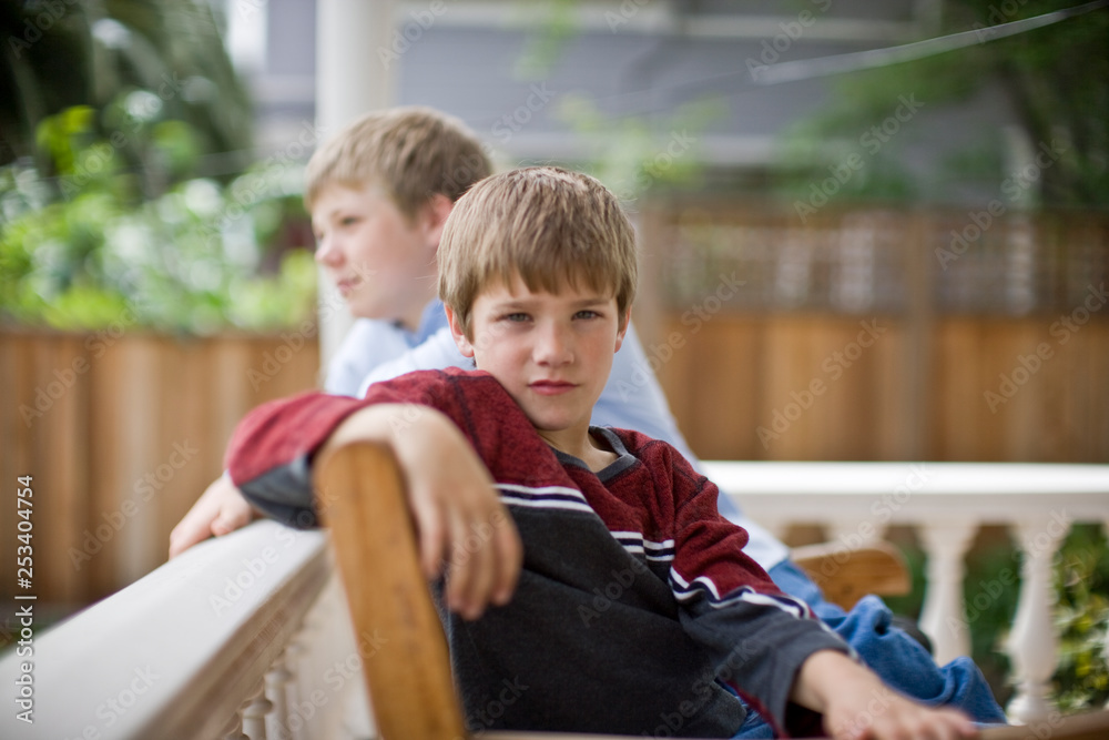 Portrait of a boy sitting with his older brother on a wooden seat on the porch of their home. Portrait of a boy sitting with his older brother on a wooden seat on the porch of their home.