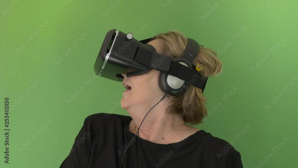Close up of a Senior Woman with headphones looking fast takes out her VR googles in green screen Close up of a Senior Woman with headphones looking fast takes out her VR googles in green screen
