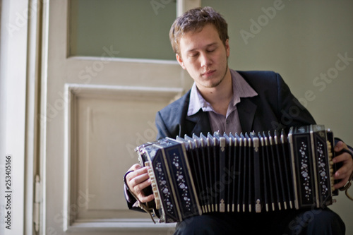 Young adult man sitting on a chair playing an accordion. photo