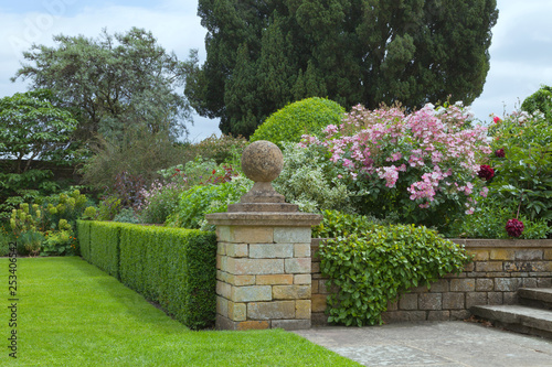 Bild auf Leinwand Landscaped garden with pink roses, flowers in bloom, shrubs and trees by trimmed hedge and stone steps