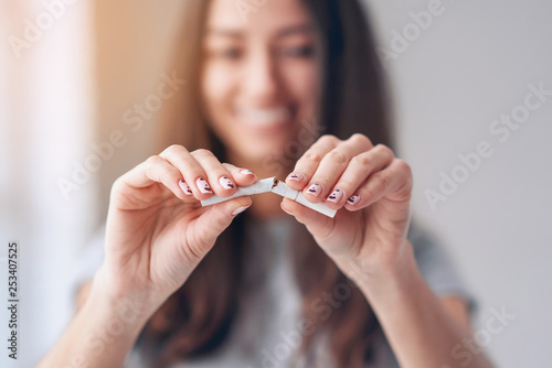Portrait of beautiful smiling girl holding broken cigarette in hands. Happy female quitting smoking cigarettes. Quit bad habit, health care concept. No smoking.