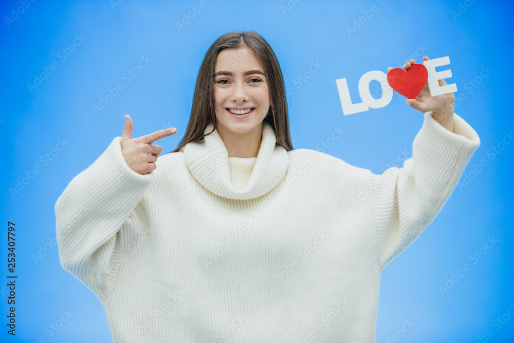Young pretty girl dressed in white clothes. During this time it stands on a blue background. Holds a word of love in hands. Young pretty girl dressed in white clothes. During this time it stands on a blue background. Holds a word of love in hands.