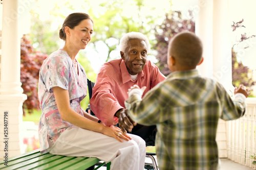 Nurse looks on happily as a senior man puts out his arms to hug a boy who is running to him for an embrace.