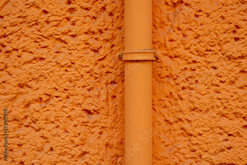 Orange verputzte Hauswand mit Rohrleitung