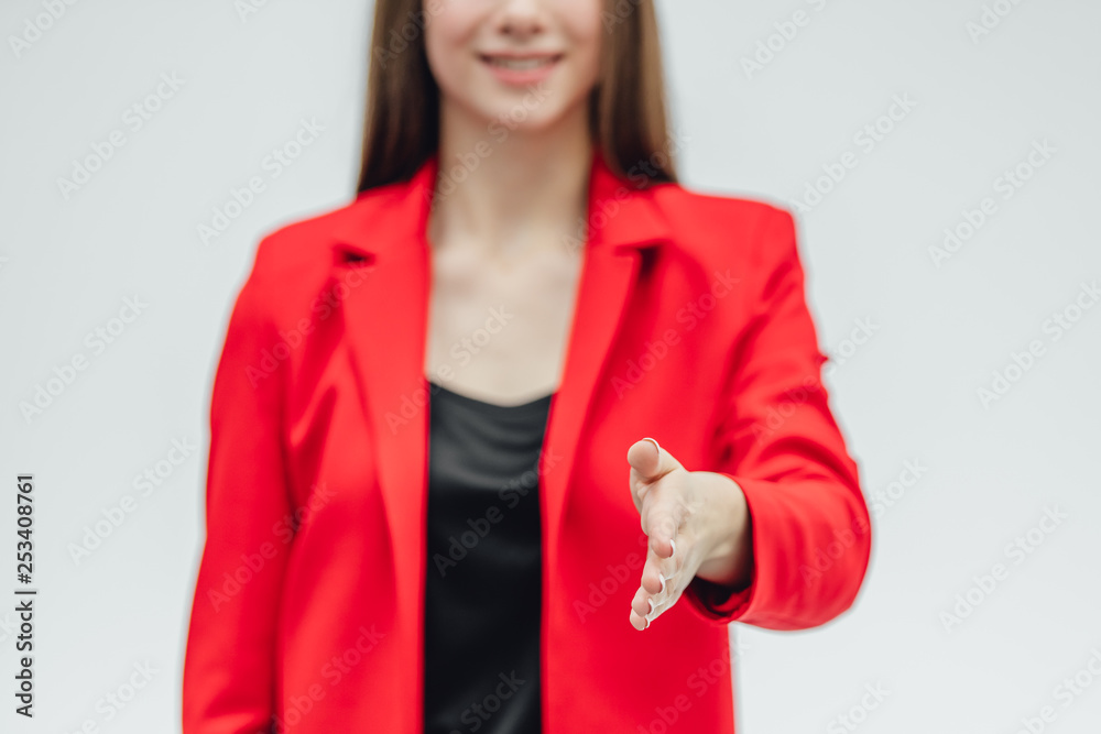 Portrait of a beautiful young brunette. Stretches your hand in congratulations. Dressed in a red jacket. Gray background. Portrait of a beautiful young brunette. Stretches your hand in congratulations. Dressed in a red jacket. Gray background.