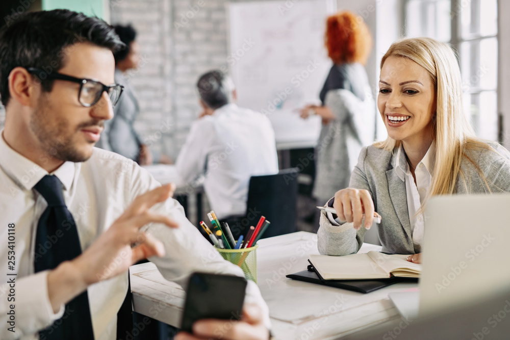 Happy businesswoman talking to her colleague while he is using mobile phone. Happy businesswoman talking to her colleague while he is using mobile phone.