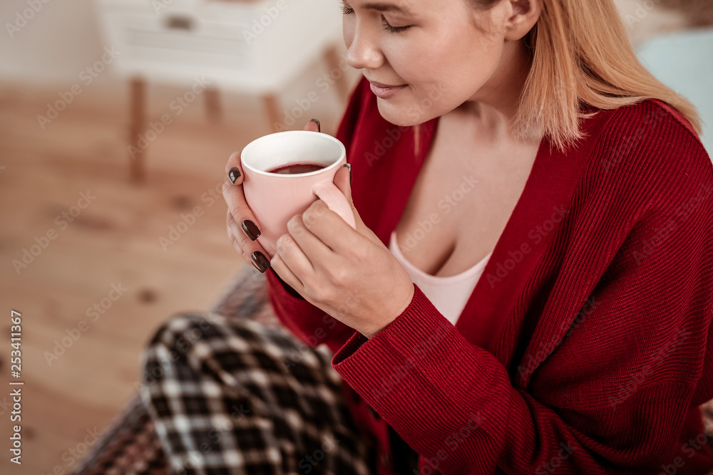 Peaceful young lady in red cardigan warming herself up