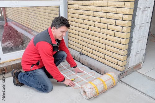 Electrician installing heating electrical cable on concrete floor.