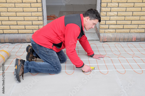 Electrician installing heating electrical cable on cement floor.