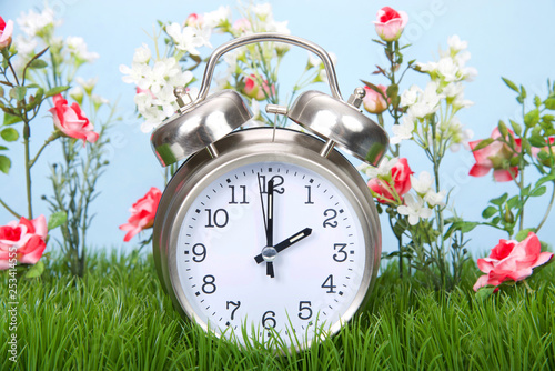 Retro style clock sitting in green grass with flowers representing daylight savings spring forwards.