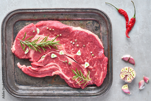 Raw steak. Meat with garlic, pepper and rosemary im metal tray, flat lay photo