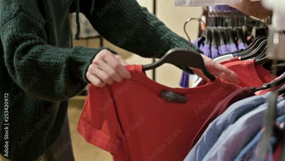 A girl in a green sweater and a yellow hat walks through a store of things and chooses what to buy. Touches things on hangers and looks at price tags A girl in a green sweater and a yellow hat walks through a store of things and chooses what to buy. Touches things on hangers and looks at price tags