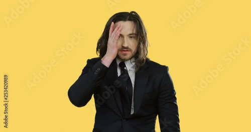 Portrait shot of the handsome young Caucasian man with long hair in the suit and tie looking very tired while standing on the yellow background. photo