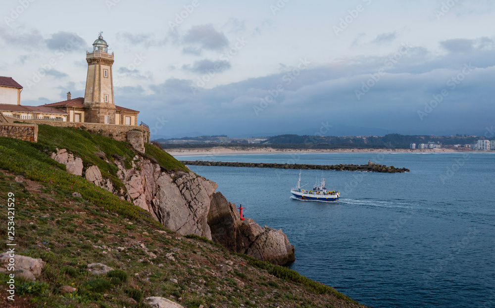 Fishing boat entering during sunset,sailing in front of the lighthouse of Saint Juan, to the port
