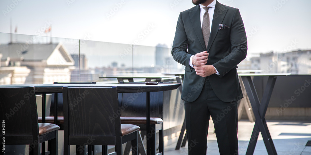 Man in expensive custom tailored suit standing and posing outdoors on balcony