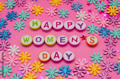 Happy Women's Day made from colorful letters and little colorful flowers against pink background