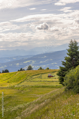 A farmer tractor on the slopes of Seiser Alm with Sassolungo Langkofel Dolomite, Alpe Di Siusi in Italy © SkandaRamana